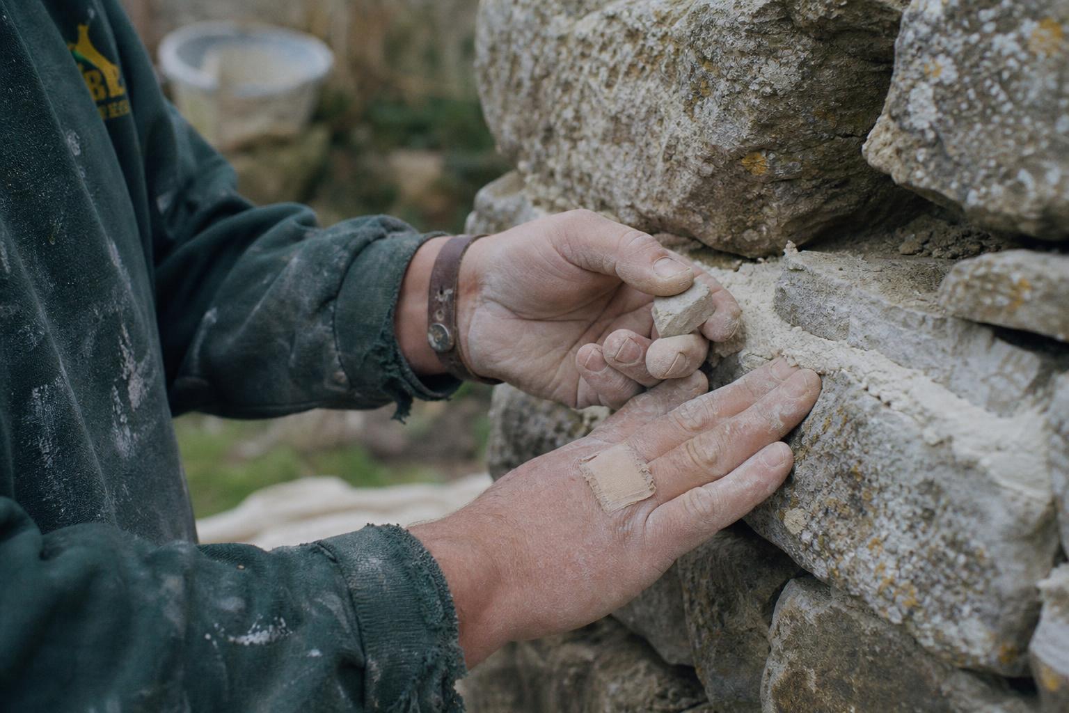 A conservator's hands at work on a stone wall